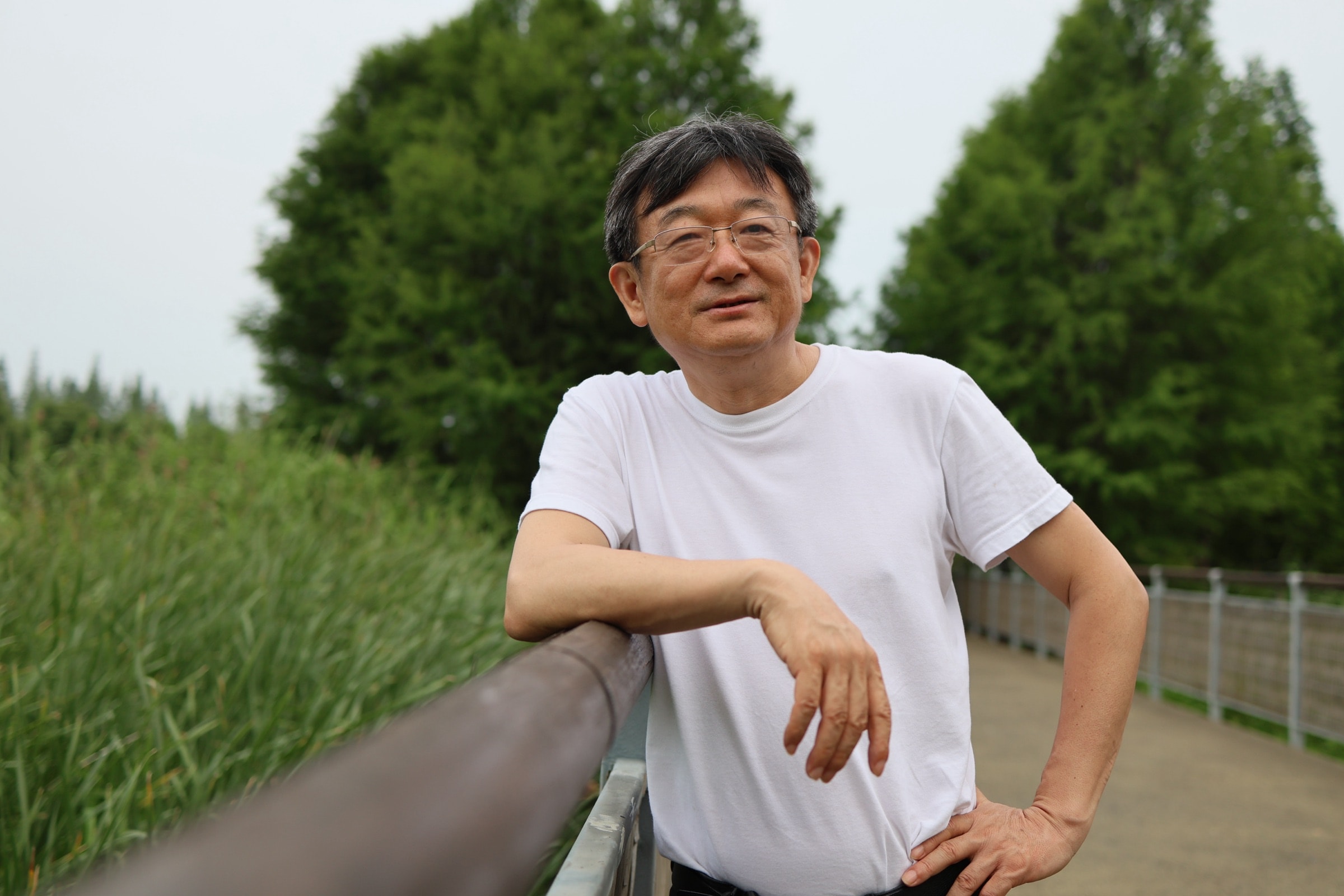 任东风身穿白色短袖上衣,站在水边步道的栏杆旁